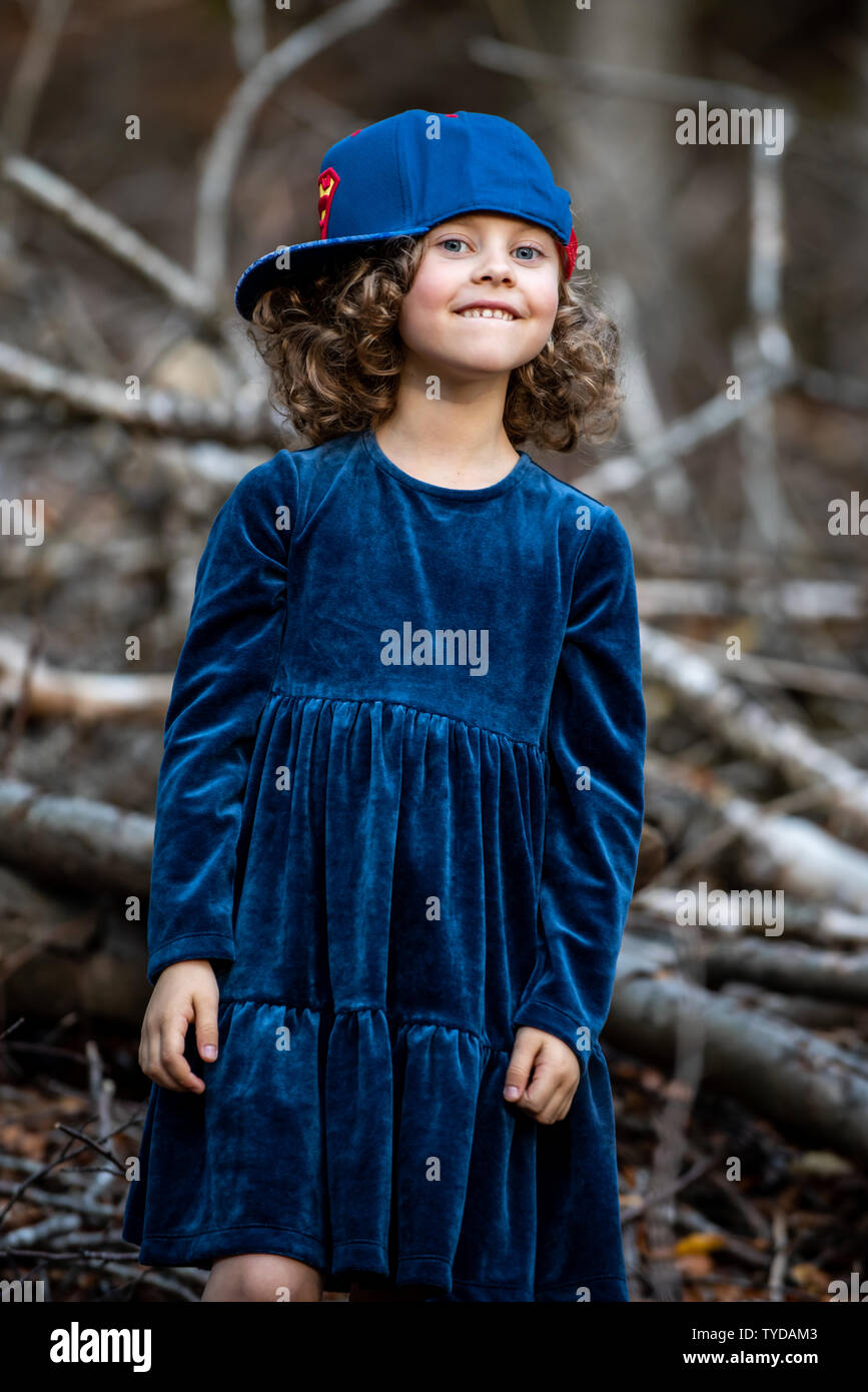 Stilvolle kind Mädchen 6-7 Jahre alt tragen Designer Blue Velvet Dress in Wald. Im Freien. Standortwahl und Kamera. Kindheit. Stockfoto