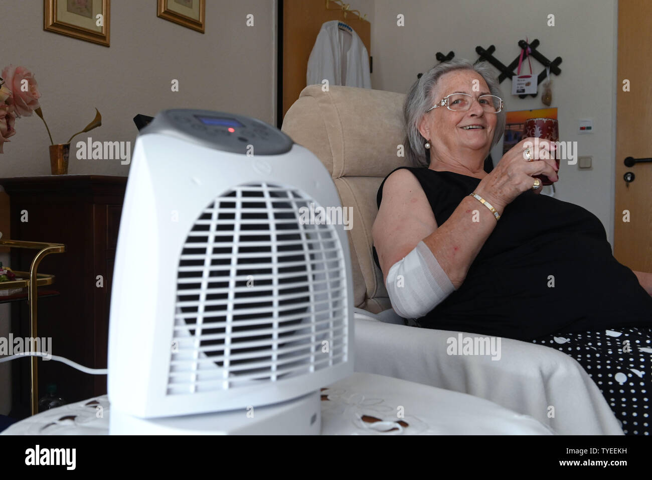 Kassel, Deutschland. 26 Juni, 2019. 76 jaehrige Renate Stössel sitzt in ihrem Zimmer im Altenheim Käthe-Richter-Haus neben einem laufenden Lüfter mit einem Glas Wasser in der Hand und versucht, die Hitze zu überstehen. Quelle: Uwe Zucchi/dpa/Alamy leben Nachrichten Stockfoto