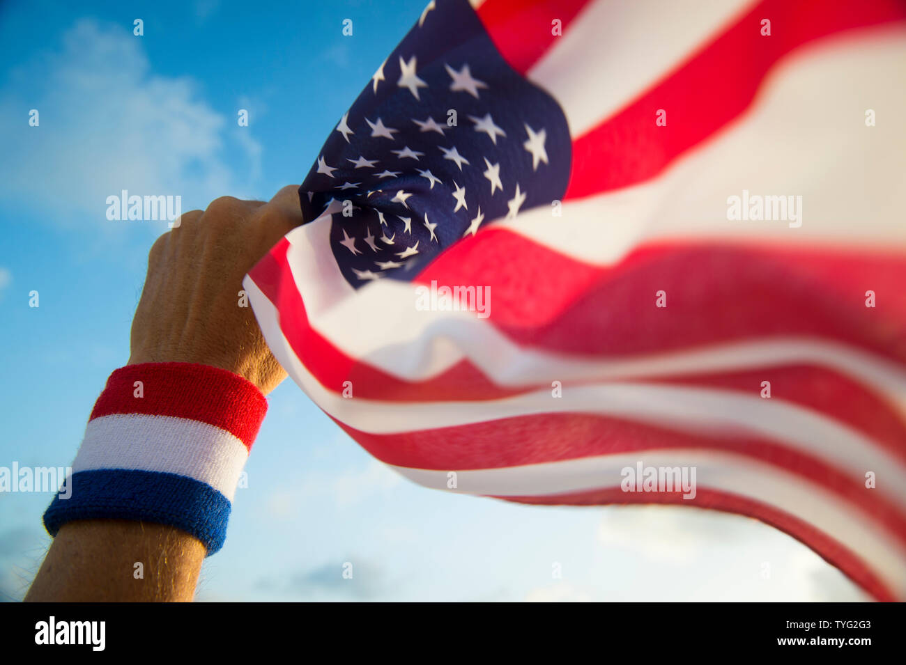 Hand mit USA rot, weiß und blau Armband Holding eine amerikanische Flagge schwenkten in hellen, sonnigen blauen Himmel Stockfoto