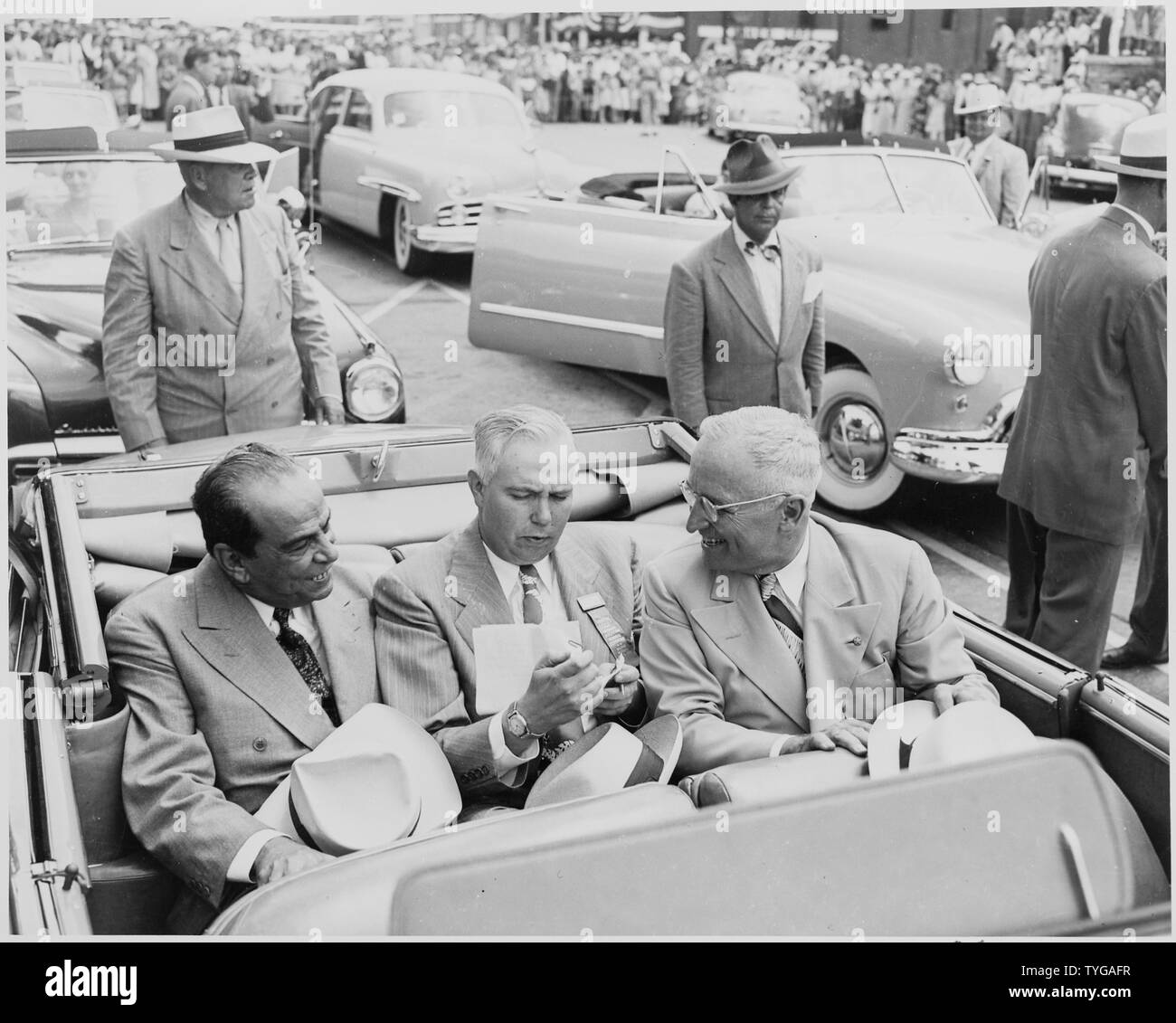 Präsident Harry S. Truman, Präsident Romulo Gallegos von Venezuela, und ein unbekannter Mann sitzt in einem Cabrio, mit anderen Autos und eine Masse im Hintergrund, in Bolivar, Missouri. Präsident Truman eine Statue von Simon Bolivar in Bolivar gewidmet. Stockfoto
