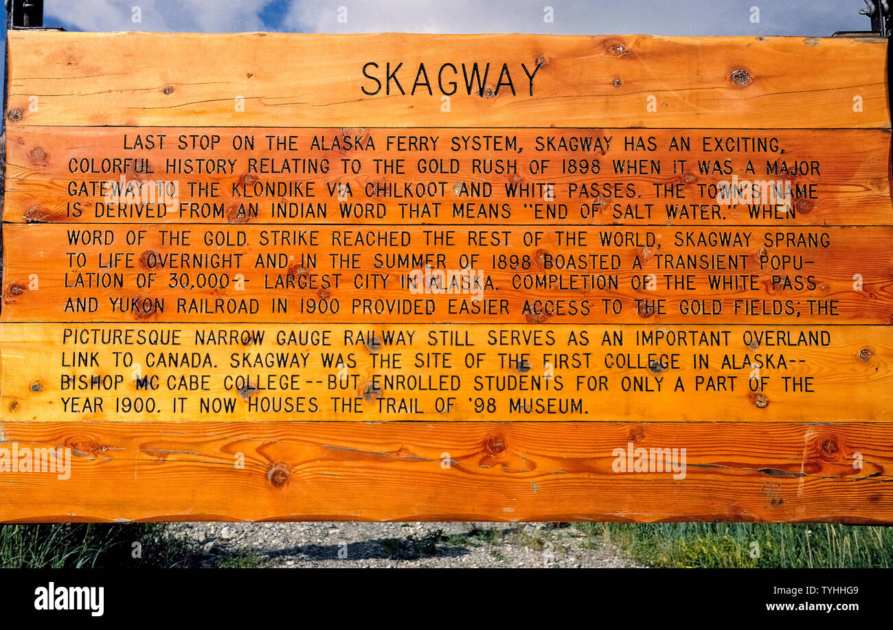 Eine hölzerne Zeichen beschreibt eine kurze Geschichte von Skagway, Alaska, USA, einem abgelegenen Außenposten berühmt durch die 1897-98 Gold Rush zu den Klondike im Yukon Territory in Kanada gemacht. Heute ist es eine beliebte Touristenattraktion von Kreuzfahrtschiffen und Fähren des Alaska Marine Highway System, das ein zu den Gemeinden im Südosten Alaskas, die keinen Zugriff auf der Straße wurden bietet erreicht. Viele Besucher nach Skagway an Bord des historischen gold-rush White Pass & Yukon Eisenbahn Für eine malerische Berglandschaft Zug Ausflug, von Meeresspiegel steigt auf den 2.915 Fuß (888 Meter) Gipfel des White Pass. Stockfoto