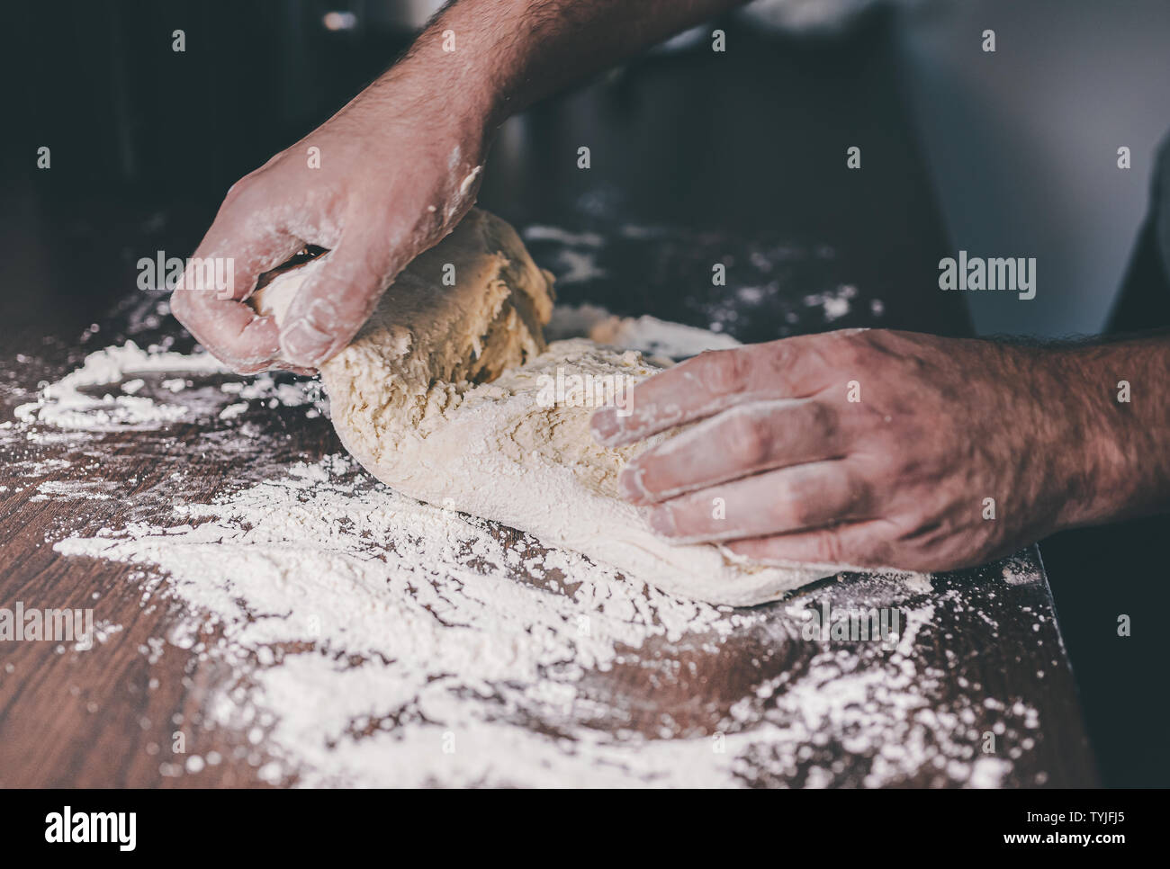 Nahaufnahmen der Hände des Menschen beim Kneten von Teig auf der Bemehlten Arbeitsplatte in der Küche Stockfoto