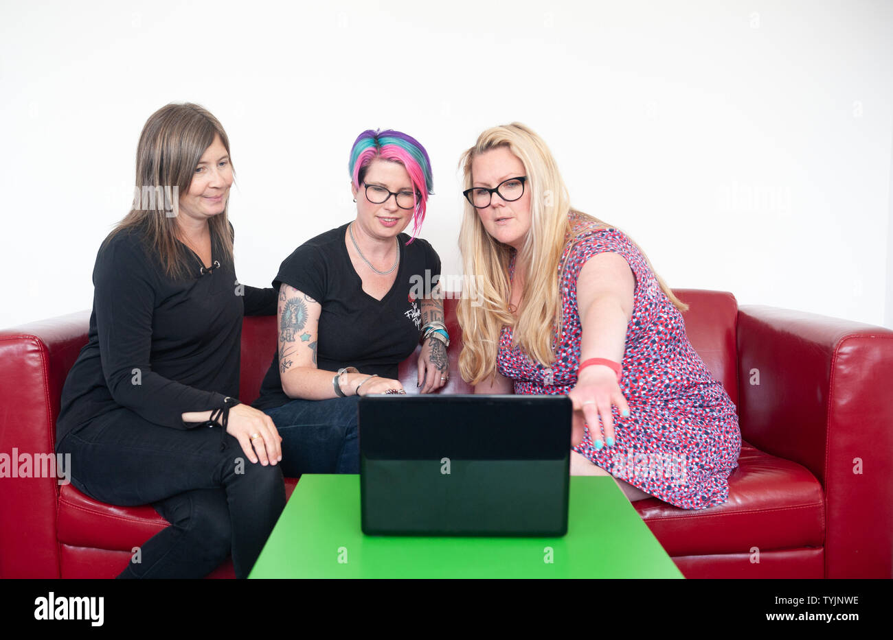 Drei Frauen auf dem roten Sofa in der Diskussion mit Laptop, weißer Hintergrund Mauer, Platz für Kopie Stockfoto