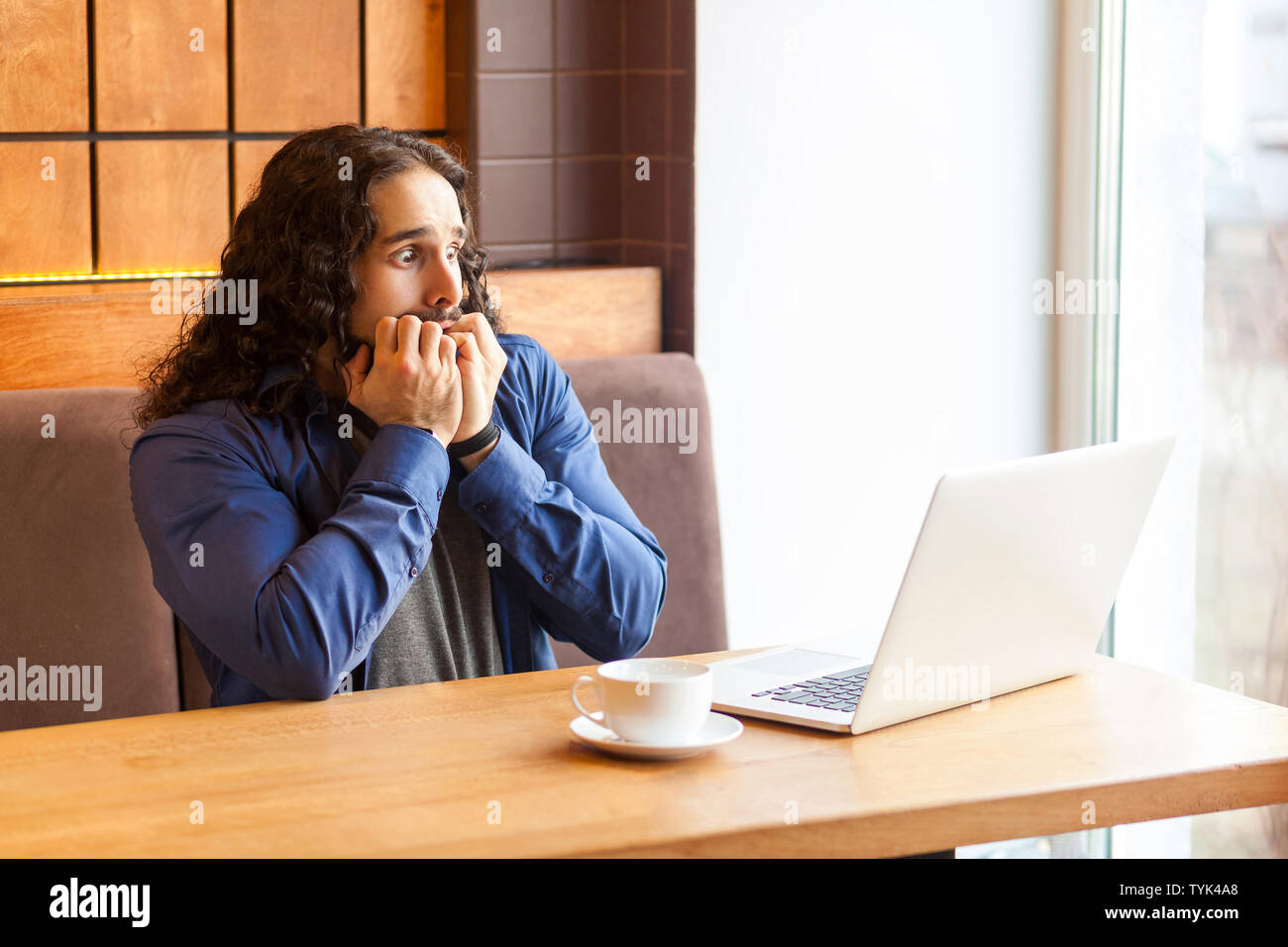 Portrait von Angst hübscher junger erwachsener Mann Freiberufler in lässigen Stil im Cafe sitzen und beobachten, Horror Film in Laptop, Beißen, Nägel, bussinessman Stockfoto