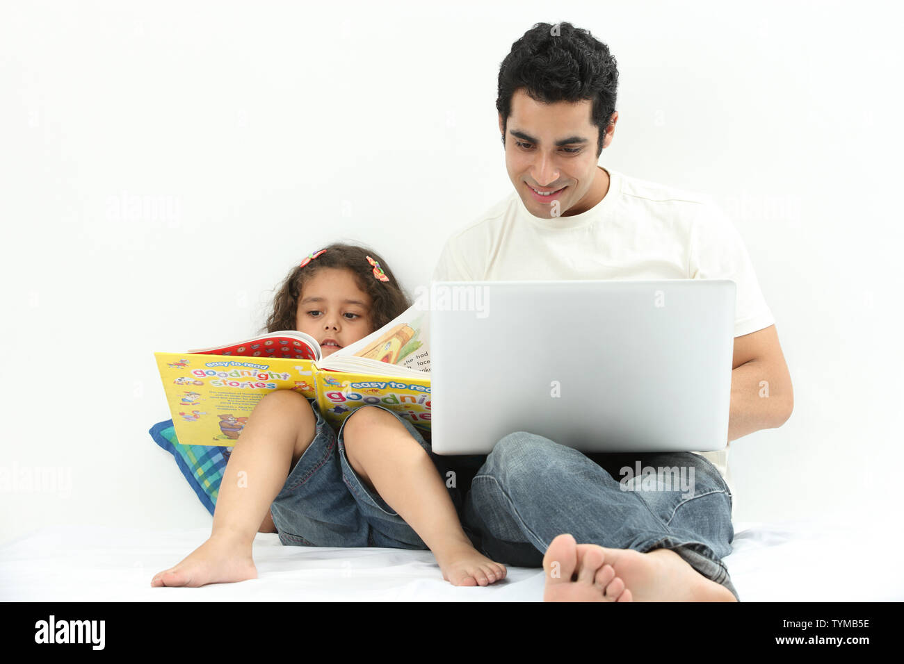 Mann mit Laptop und seiner Tochter, die neben ihm ein Buch liest Stockfoto