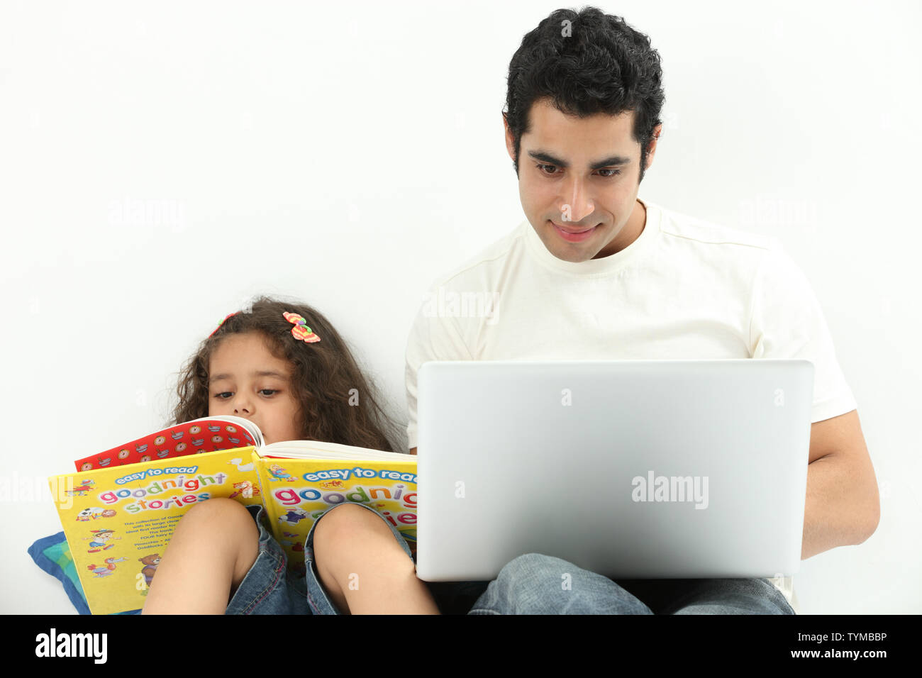 Mann mit Laptop und seiner Tochter, die neben ihm ein Buch liest Stockfoto