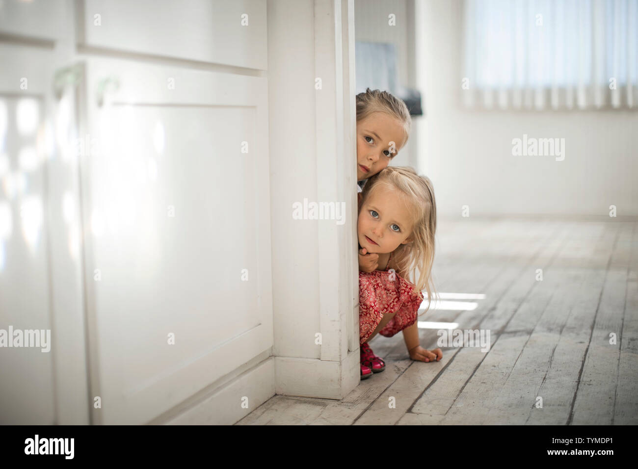 Zwei junge blonde Schwestern Peek um die Kante des Türrahmens. Stockfoto