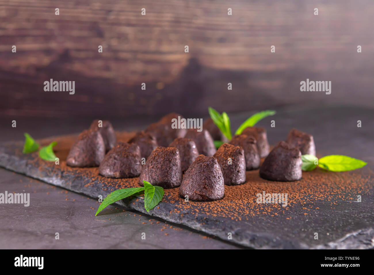 Hausgemachte Schokolade Trüffel mit Minze bestreut mit Kakaopulver auf Schiefer. Fokus auf erste Trüffel. Stockfoto