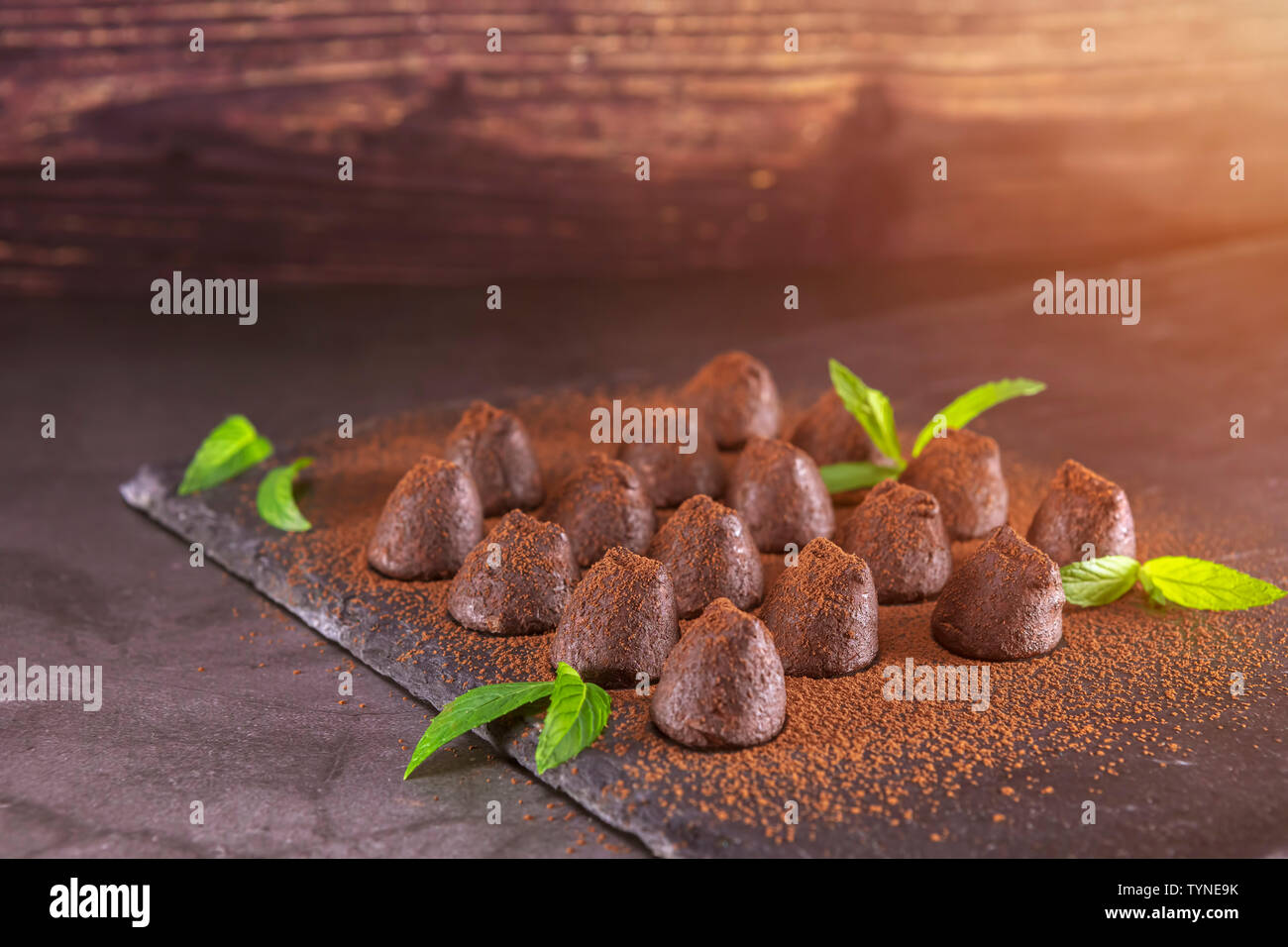 Hausgemachte Schokolade Trüffel mit Minze bestreut mit Kakaopulver auf Schiefer. Fokus auf Trüffeln Stockfoto