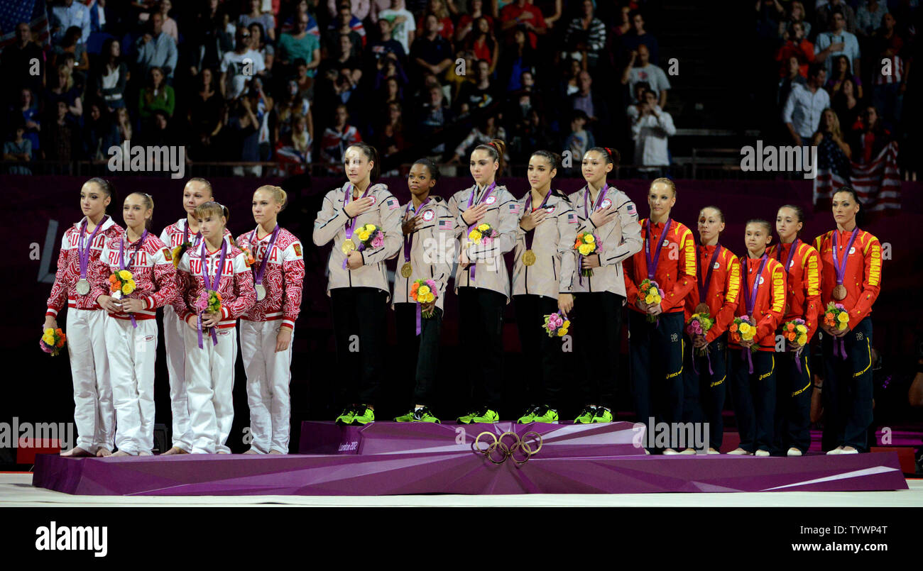 Die Nationalhymne der USA gespielt als die Goldmedaillenträger zusammen mit Silber Medaillengewinner Russland (L) und Bronze- medaillengewinner Rumänien Gymnastik Team der Damen an der North Greenwich Arena während der Olympischen Sommerspiele 2012 in London in Greenwich, London Am 31. Juli 2012 hören. UPI/Pat Benic Stockfoto