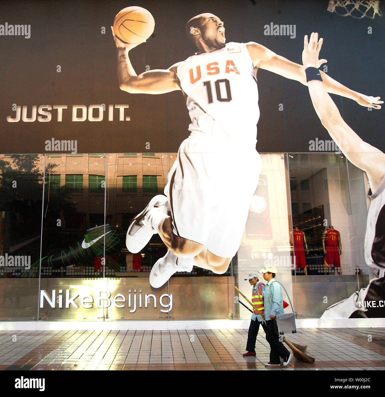 Chinesische Straßenreinigung Spaziergang, vorbei an einem riesigen reklametafeln eines USA Basketball player, über Dunk über einen Gegner zu schleudern, schmücken ein von Nike Flagship Stores nur in der Innenstadt von Peking, 13. Juli 2008 eröffnet. Peking wurde mit olympischen Fieber, mit den meisten nationalen und internationalen sportlichen Gute speichert jetzt mit olympischen Motto Werbung Verbraucher anzuziehen überwältigt. (UPI Foto/Stephen Rasierer) Stockfoto