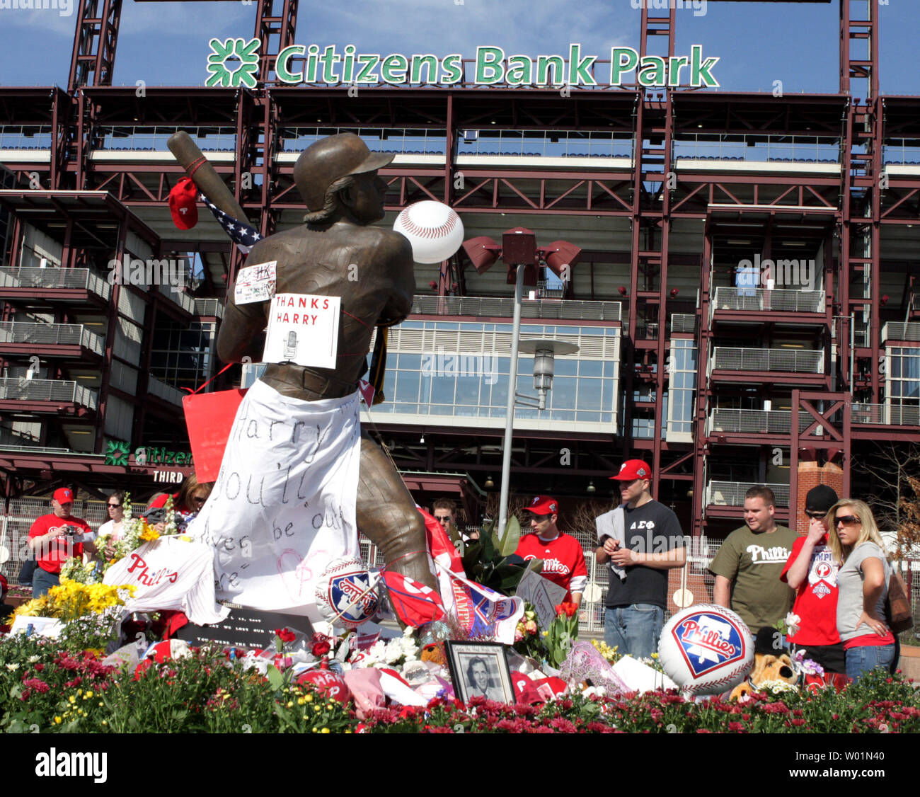 Philadelphia Phillies fans stoppen und bei den improvisierten Gedenkstätte für Fahnen, Blumen und Trikots an der Statue von Philadelphia Baseballspieler Mike Schmidt vor der Citizens Bank Park April 17, 2009 im Gedenken an den langjährigen Philadelphia Phillies Ansager Harry Kalas. Kalas, ein Philadelphia Phillies Ansager für die letzten 30 Jahre, starb vor der Phillies Spiel in Washington, 13. April 2009. Kalas wird im Zustand im Baseballstadion liegen, die erste Baseball Person so zu tun, da Baby Ruth im Jahre 1948 starb. (UPI Foto/John Anderson) Stockfoto