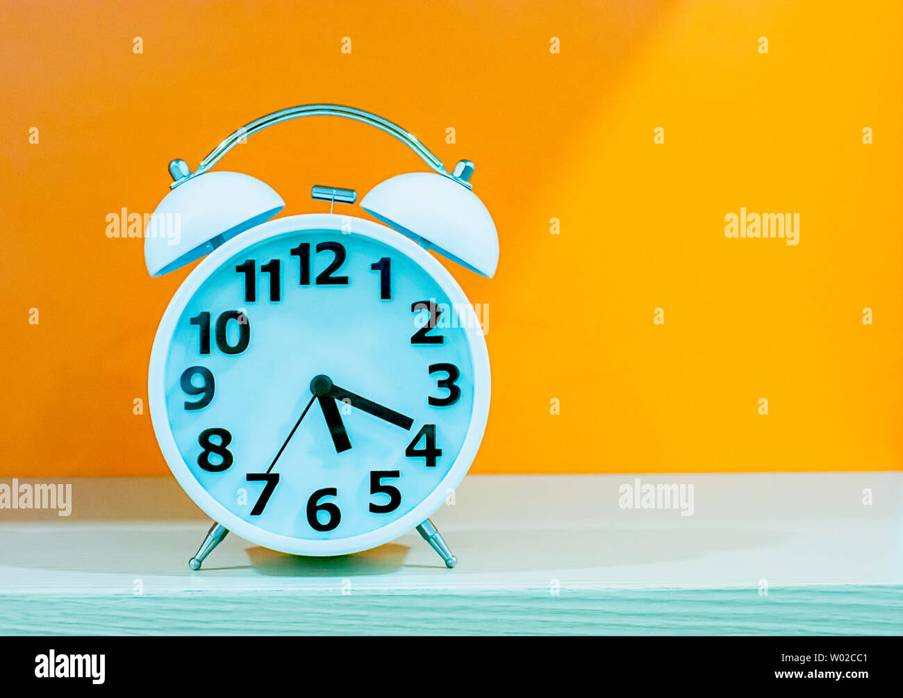 Wecker mit weißem und schwarzem Zifferblatt auf einem orangefarbenen Hintergrund. Stockfoto