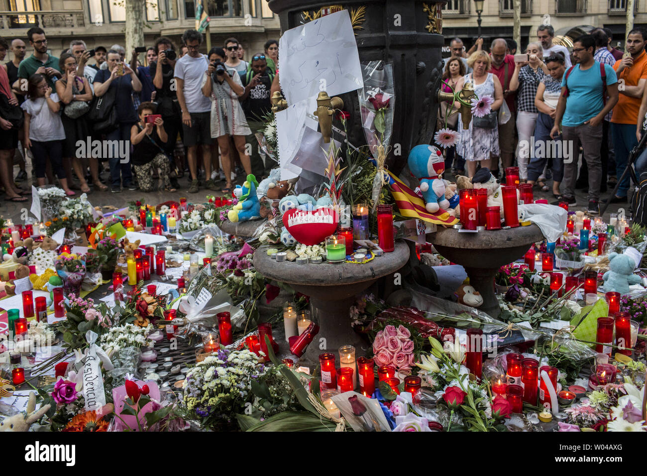 Menschen stehen neben Blumen, Kerzen und andere Gegenstände auf die Font de Canaletes in Barcelona, als Sie erinnert an die Opfer des Barcelona angriff, einen Tag nach dem van in die Menge gepflügt, 14 Personen getötet und über 100 verletzt wurden am 18. August 2017. Die Fahrer haben am 17. August 2017 gepflügt. Foto von Angel Garcia/UPI Stockfoto