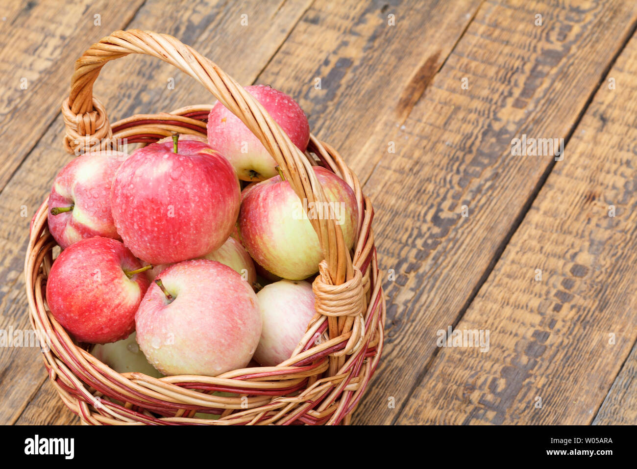 Reife äpfel mit Wassertropfen im Weidenkorb auf alten Brettern. Flache Tiefenschärfe, Ansicht von oben mit der Kopie spase. Stockfoto