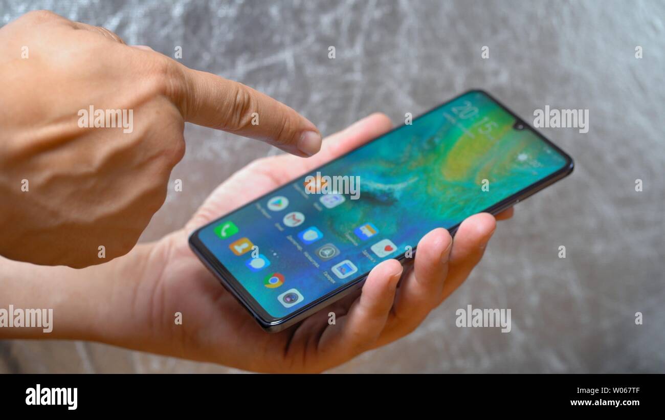 Mann mit Huawei Mate 20 X-Smartphone in der Hand und zeigte mit dem Finger  auf dem Bildschirm leuchtet grau hinterlegt. Display wird eingeschaltet,  und das Hauptmenü aktiviert Stockfotografie - Alamy