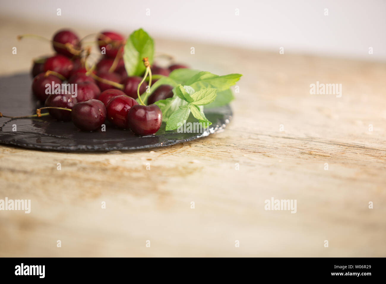 Frische Kirschen auf einem schwarzen Schild des nassen Schiefer mit Zweig frischen grünen Minze auf hellem Holz Tisch in selektiven Fokus für Kopie Raum Stockfoto