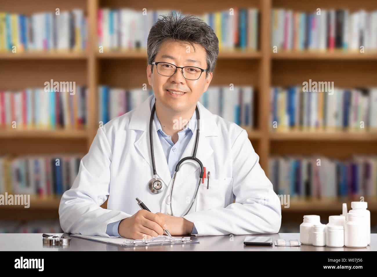 Asiatische männlicher Arzt am Schreibtisch sitzt lächelnd. Stockfoto