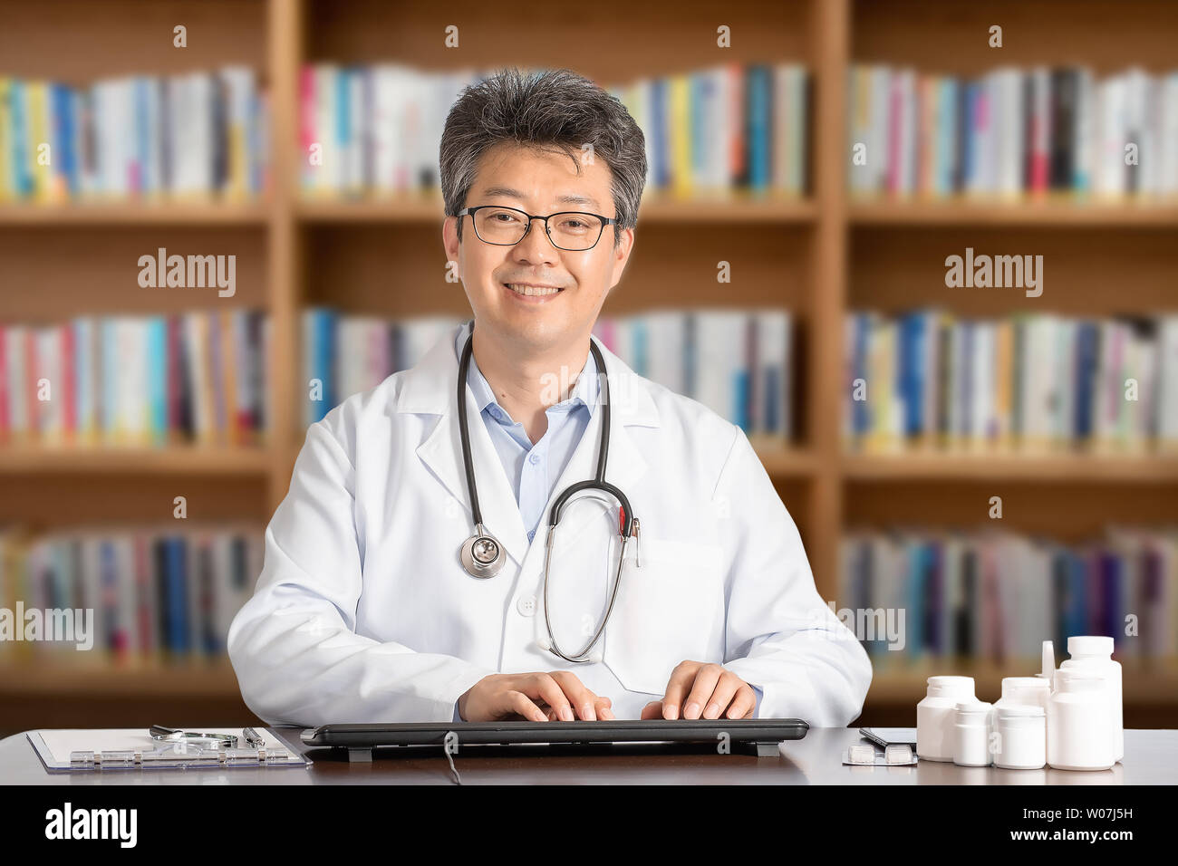 Asiatische männlicher Arzt am Schreibtisch sitzt lächelnd. Stockfoto
