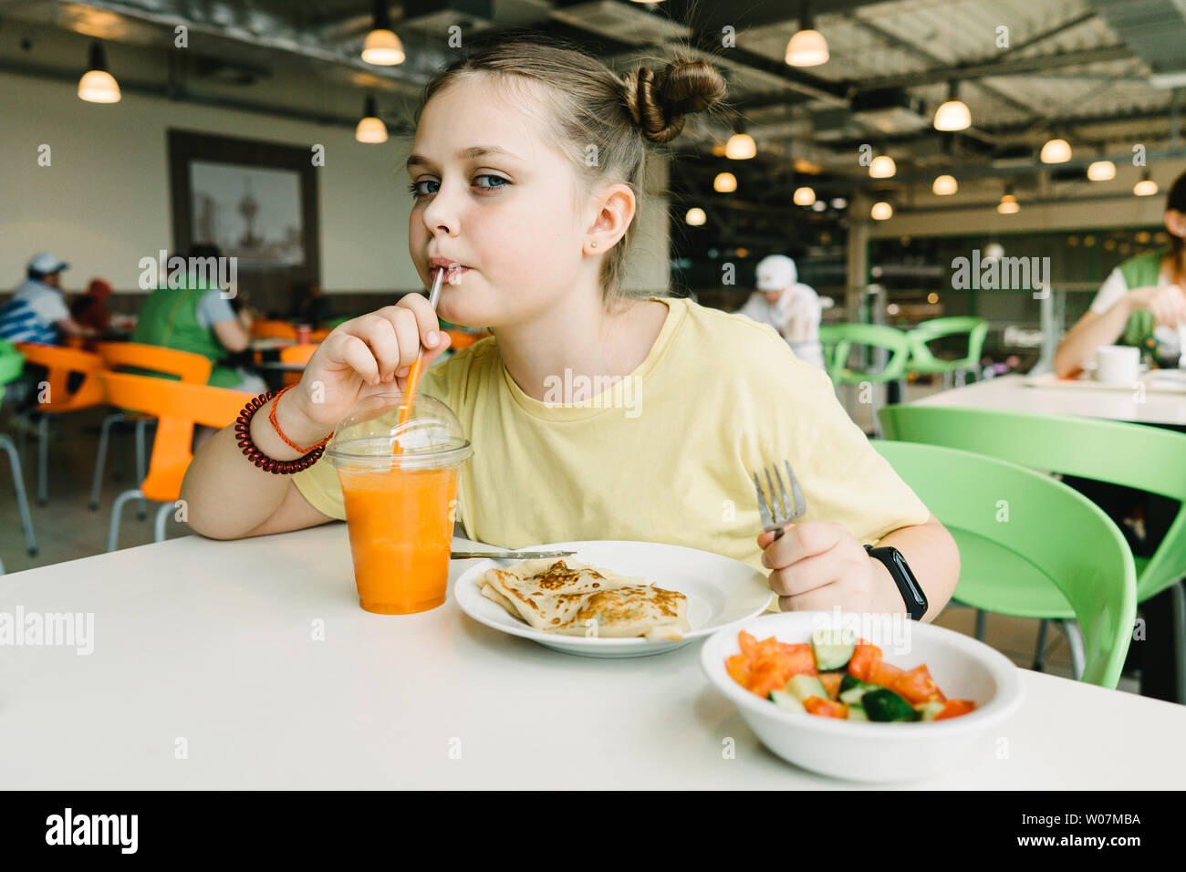 Ein jugendlicher Mädchen sitzt in einem Cafe trinken Karotten Smoothie und Pfannkuchen essen Stockfoto