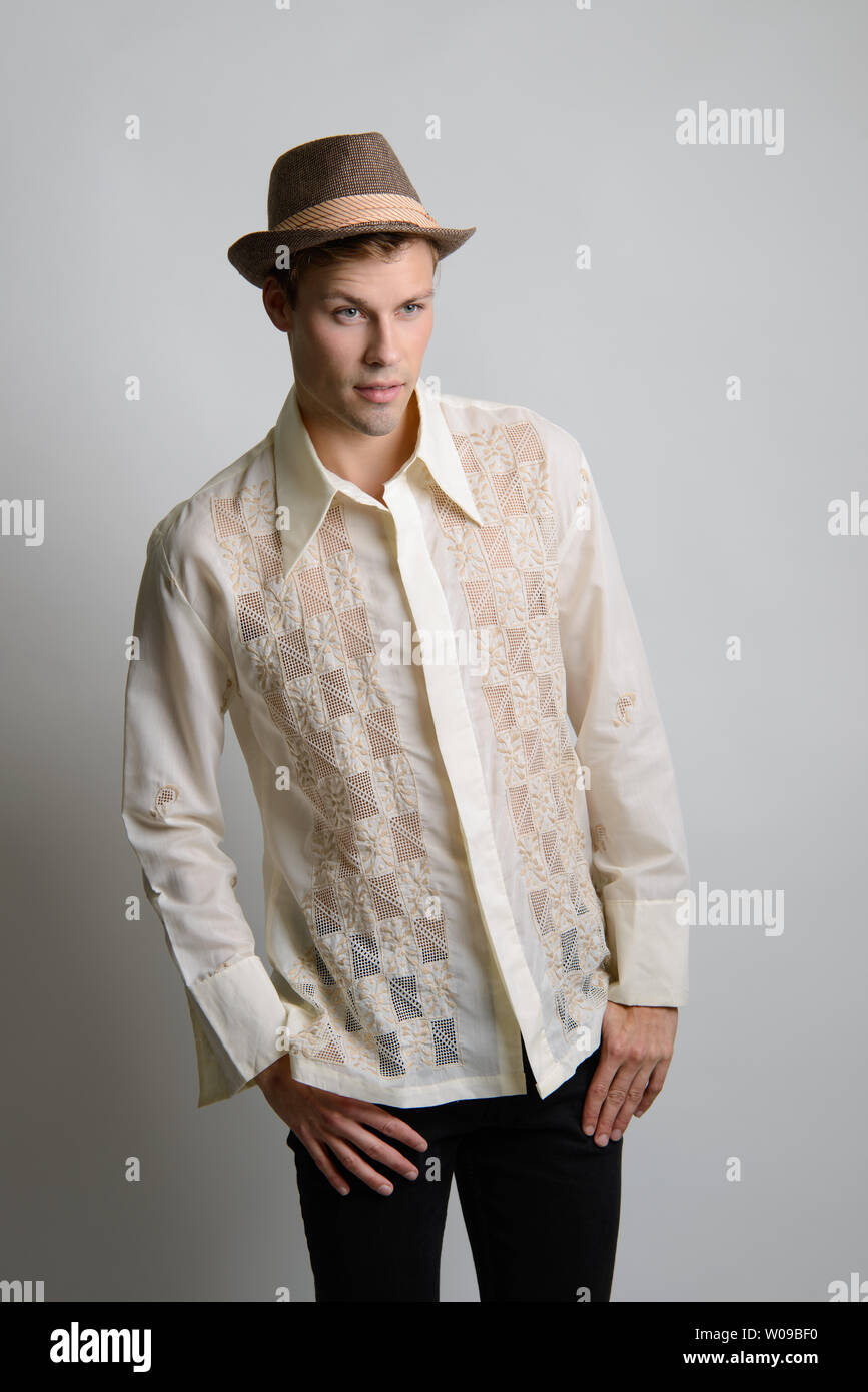 Ein gutaussehender kaukasischer Mann mit braunem Haar posiert in einem cremefarbenen Vintage 70s-Hemd und trägt einen braunen Fedora-Hut. Stockfoto
