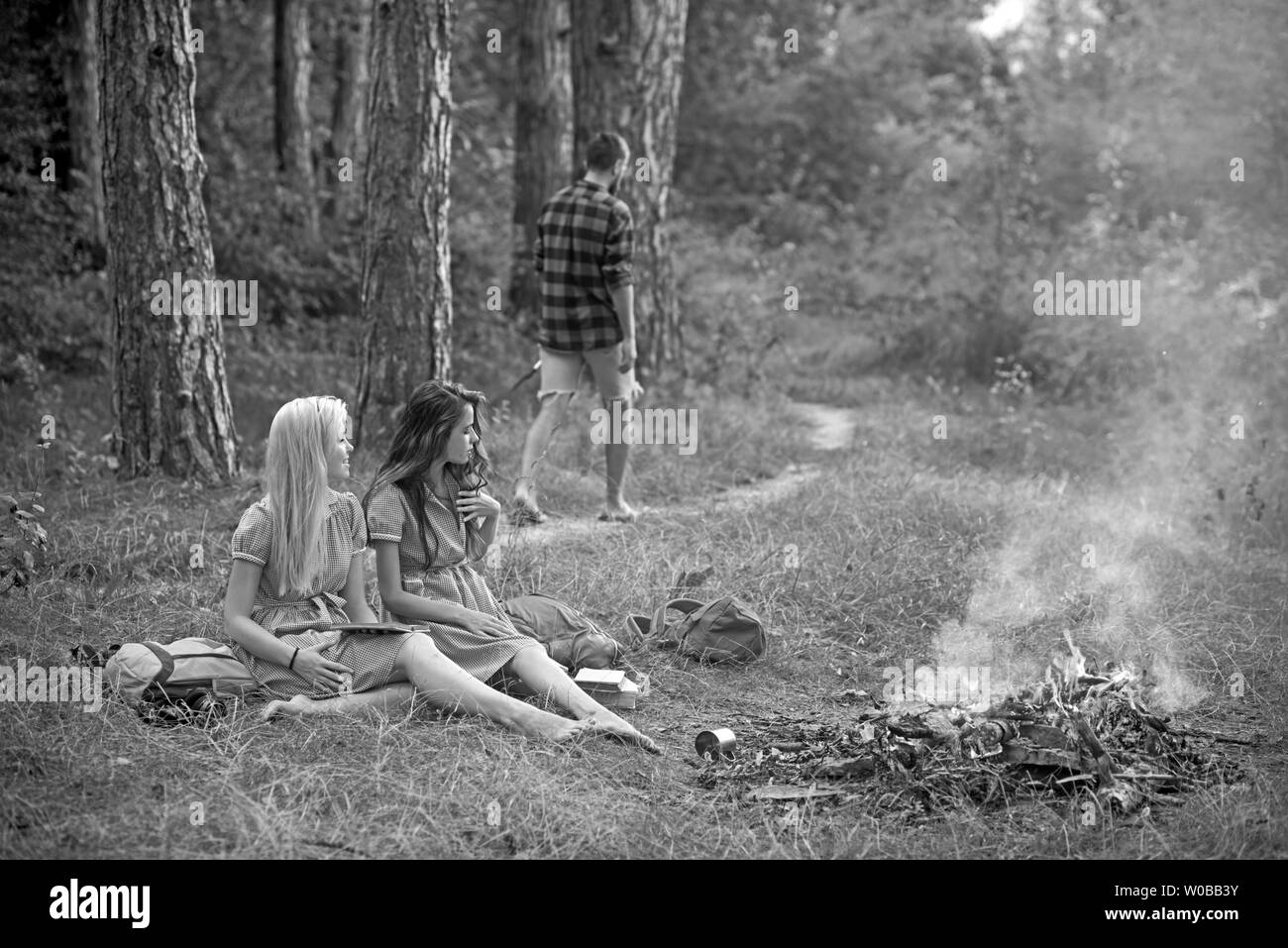 Junge Mädchen das Lesen von Büchern in Wald oder Park. Schöne Frauen sitzen am Lagerfeuer. Kerl zu Fuß auf dem Weg in den Wald Stockfoto