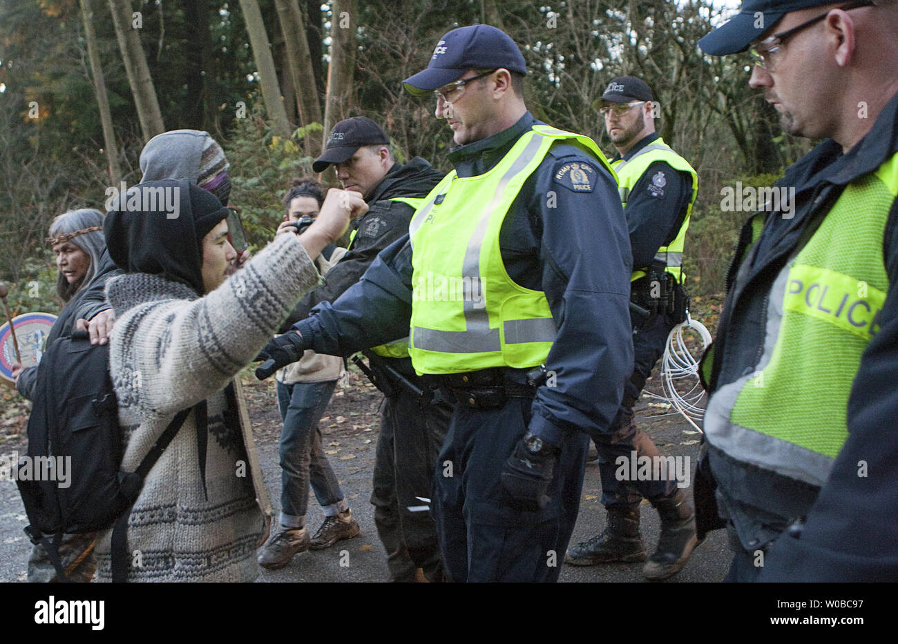 RCMP Offiziere drücken zurück David Suzuki's enkel Tamo Campos zu erlauben, ein van Last von Verhafteten abzuweichen, als über 400 Menschen stellte sich heraus, Umfrage Bohren auf Burnaby Mountain von US-amerikanischen Unternehmen Kinder Morgan für Ihre vorgeschlagene zweite Pipeline von der Alberta tar sands nach Vancouver, British Columbia am 23. November 2014 zu protestieren. Über 60 Menschen wurden seit Donnerstag, wenn rcmp Polizisten begannen Durchsetzung einer v. Chr. Oberste Gerichtshof einstweilige Verfügung gegen Kinder Morgan Demonstranten festgenommen. UPI/Heinz Ruckemann Stockfoto