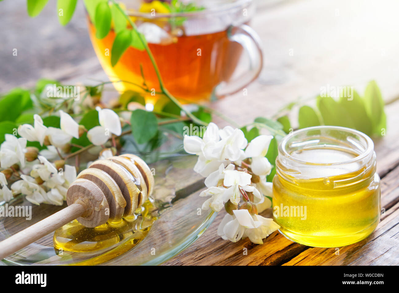Akazie blumen Honig Glas, Holz- Pendelarm und gesunde Kräuter Tee Tasse. Stockfoto