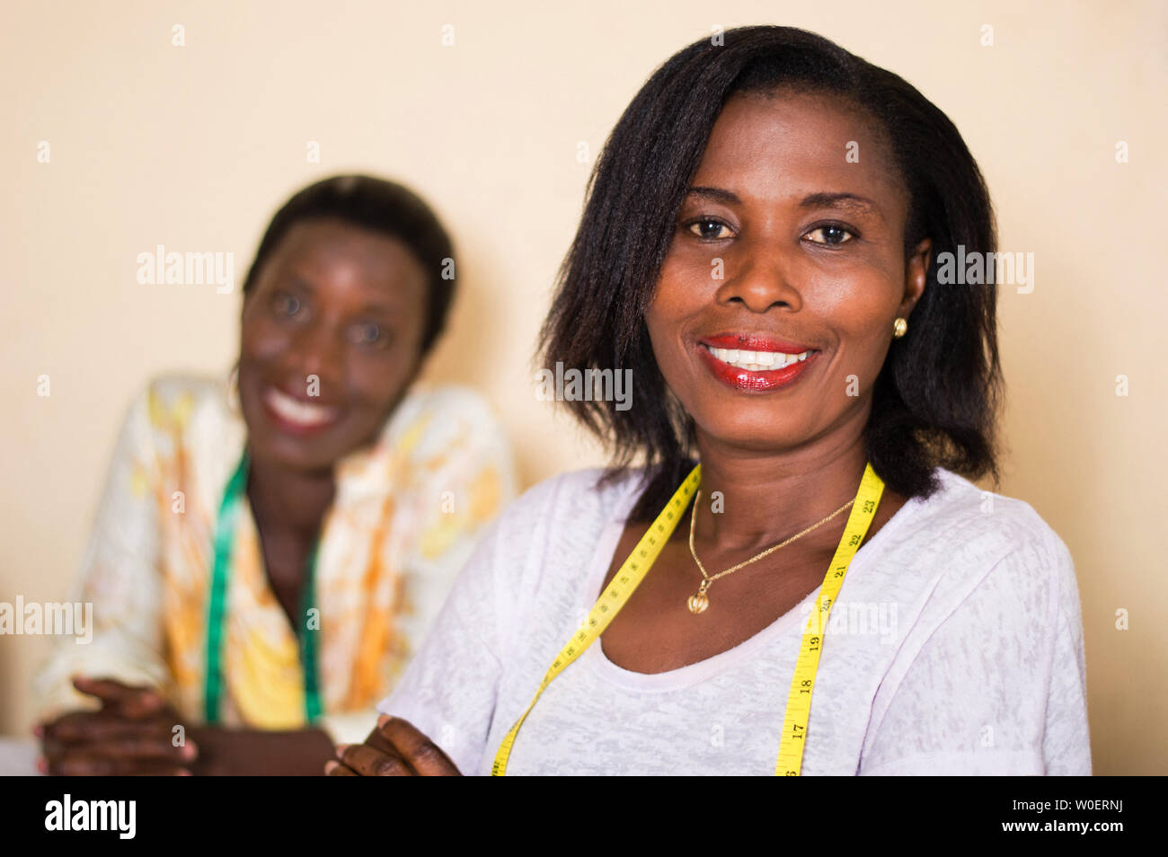 Lächelnd Näherin in ihrer Werkstatt schaut in die Kamera mit ihrer Kollegin im Hintergrund. Stockfoto