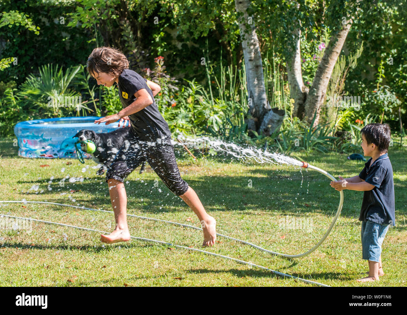 Zwei Jungen von 4 Jahren und 12 Jahren spielen mit einem Schlauch im Garten Stockfoto