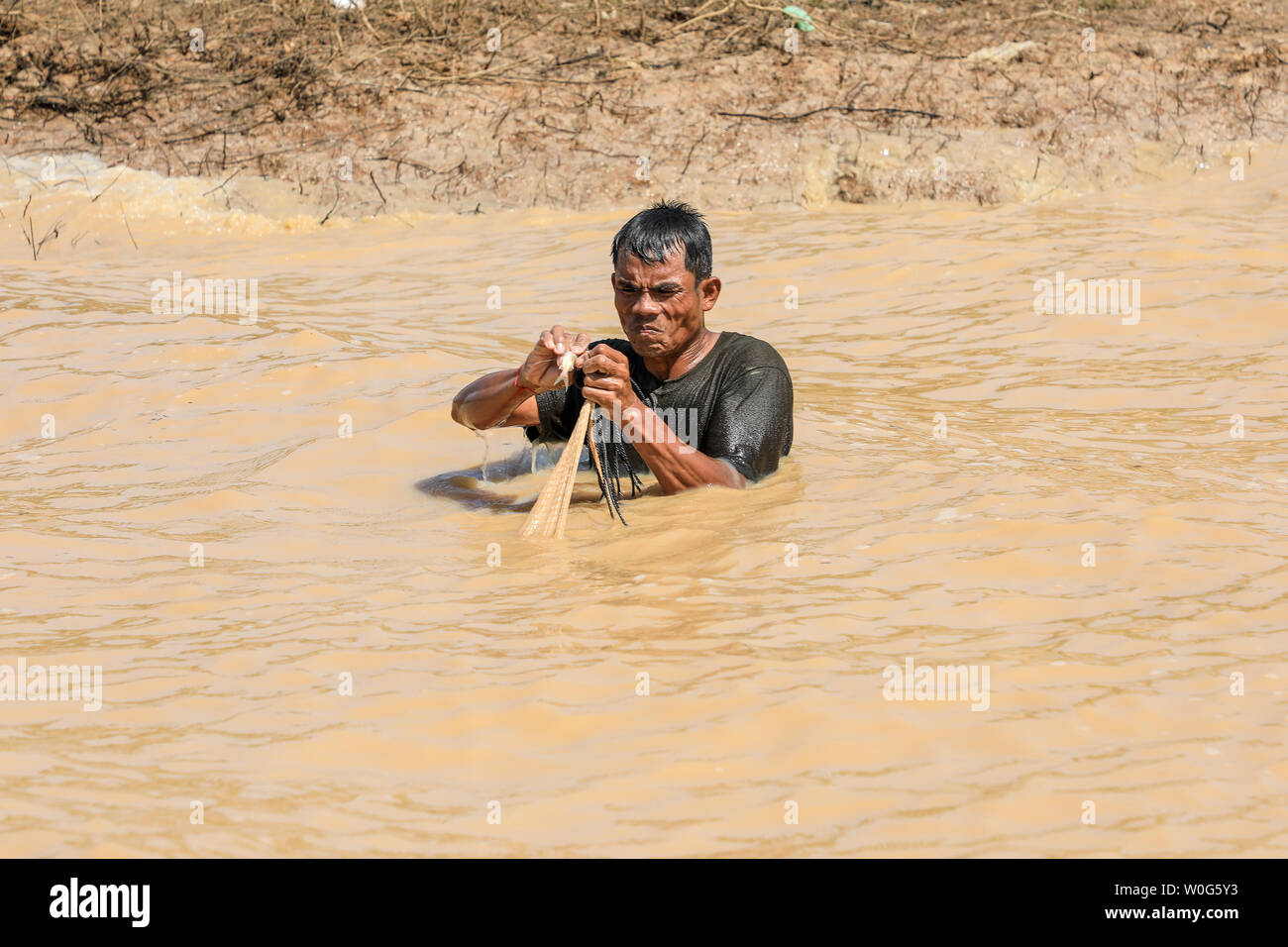 Ein Fischer, Brust tief im Fluss, der Befreiung der Fisch aus seine Netze Tonlé Sap Fluss, Tonlé Sap See, in der Nähe von Siem Reap, Kambodscha, Südostasien Stockfoto