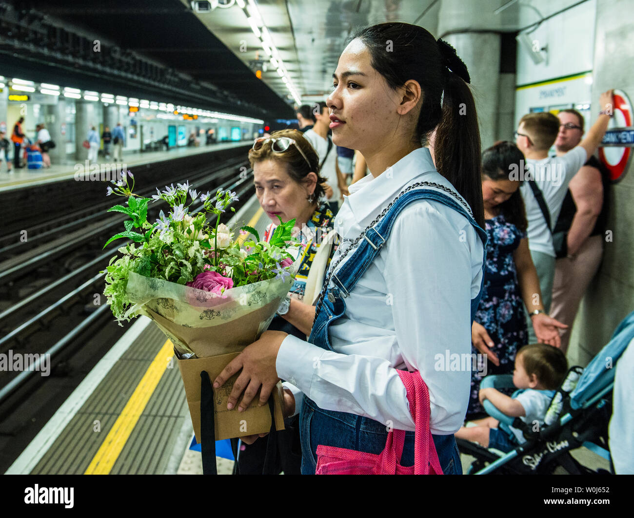 Junge Frau zum Zug auf u-Plattform mit Blumen, London, England, Großbritannien Stockfoto