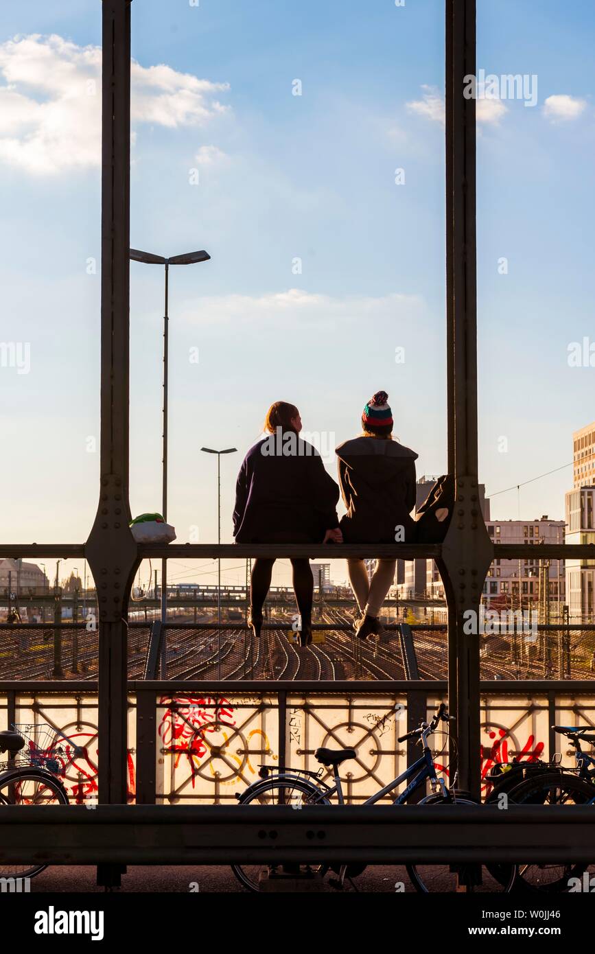 Zwei junge Frauen sitzen auf dem Geländer der Haccurbrucke Brücke über die Gleise in die Ferne, Back Light, München suchen, Obere Stockfoto