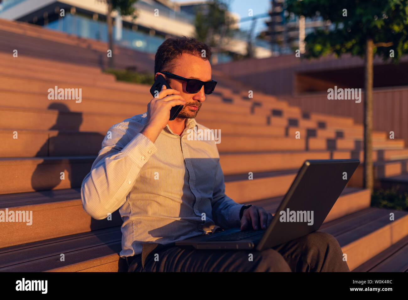 Seitenansicht Portrait von Young Business Executive Aufruf auf Smartphone und mit Laptop im Freien. Stockfoto