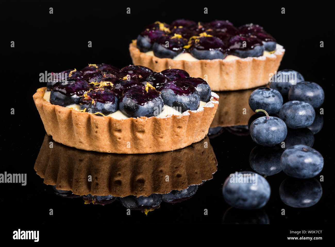 Zwei Blaubeere und Pudding mit frischen Blaubeeren auf schwarzem Granit mit Reflexionen Stockfoto