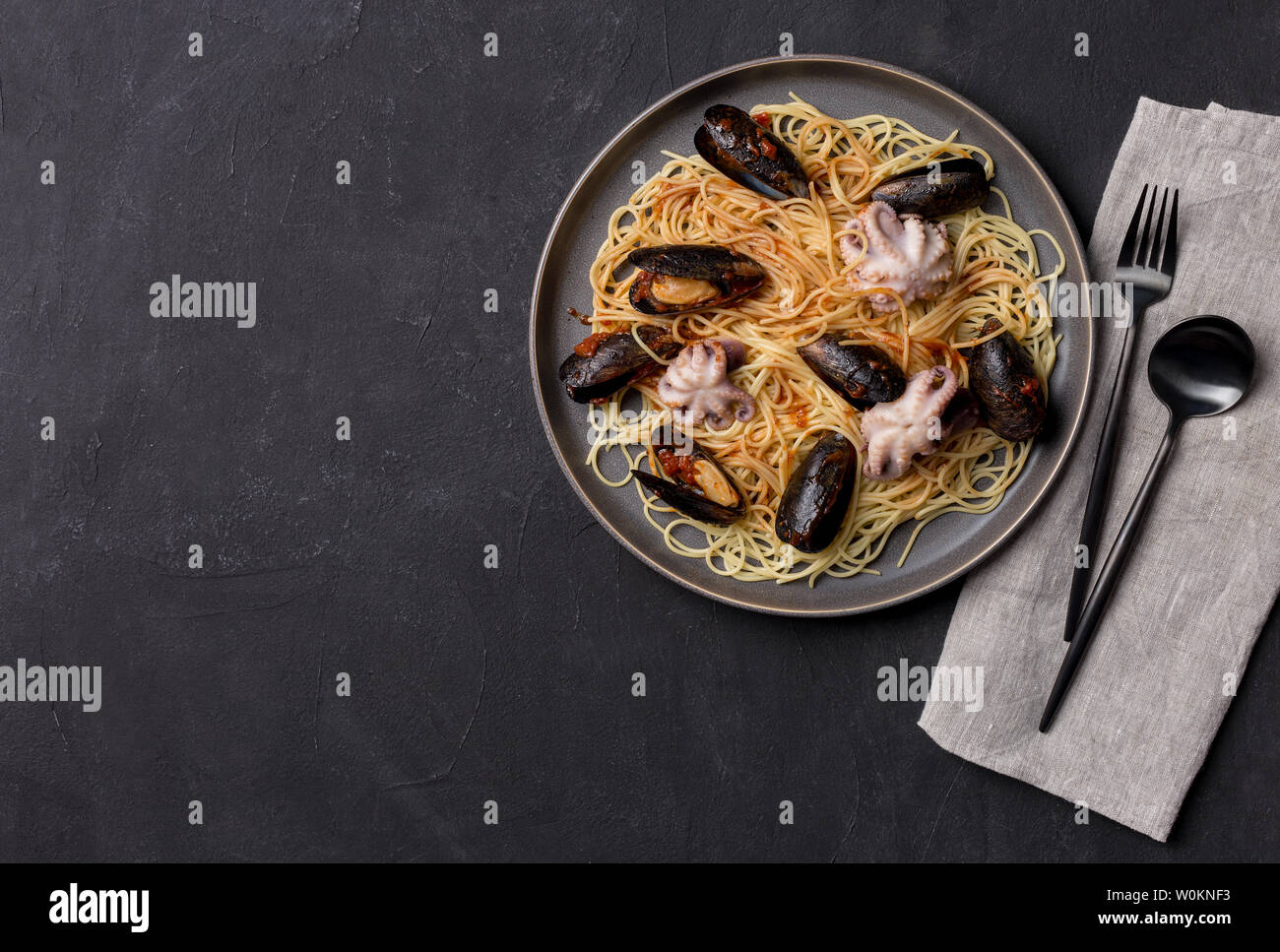 Spaghetti mit Muscheln und Tintenfisch in graue Platte mit Geschirr und Servietten auf schwarzem Hintergrund. Ansicht von oben flach, freier Speicherplatz Stockfoto