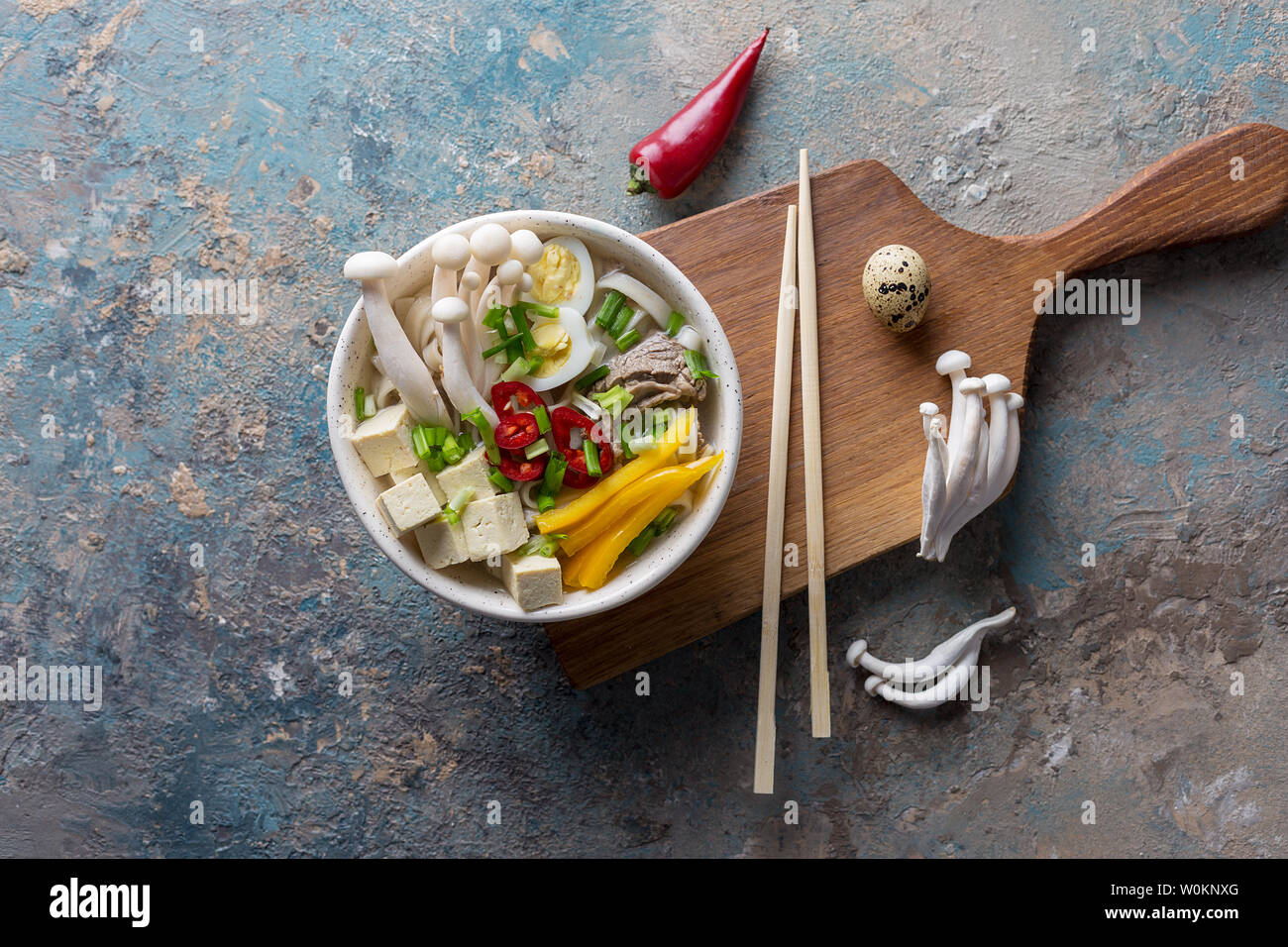 Nudeln mit Pilzen und Gemüse in der Schüssel. Paprika, gelb Paprika, Tofu, Zwiebeln, gekochtem Rindfleisch und Chinesische Pilze auf konkreten Hintergrund. Ansicht von oben f Stockfoto