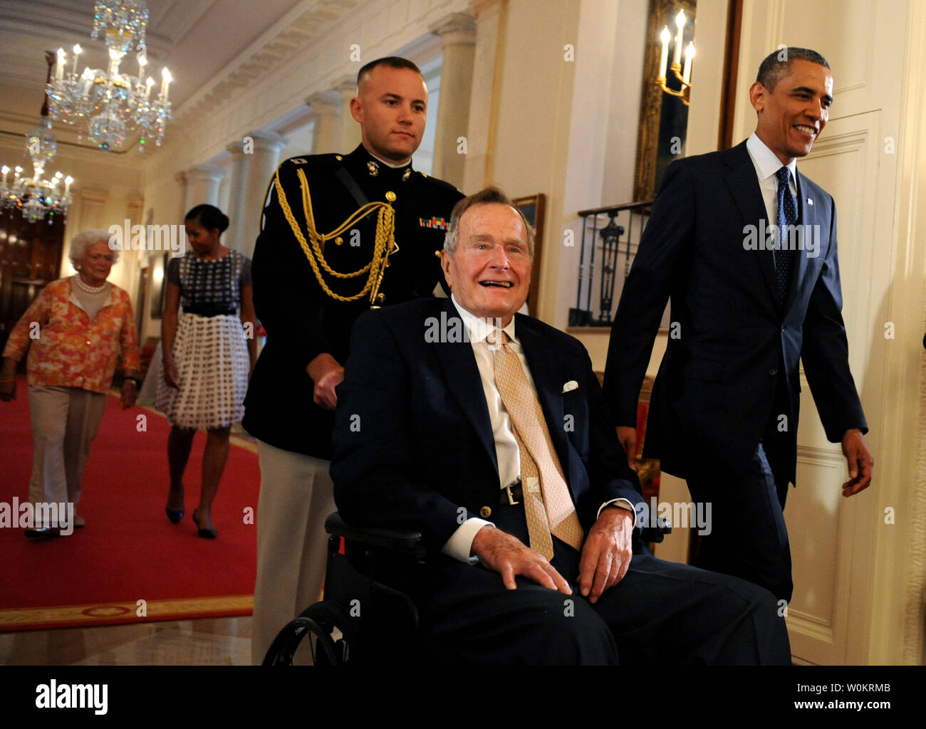 Us-Präsident Barack Obama geht mit ehemaliger Präsident George H.W. Bush im Osten Zimmer des Weißen Hauses zu den 5.000 th Award von Bushs 'Points of Light Foundation in Washington, DC am 15. Juli 2013 vorlegen. Bush hat die nationale Bewegung volunteerism und Dienst an der Gemeinschaft zu Vorauszahlung vor 20 Jahren, als er die 41. Präsident war. Im Hintergrund sind der First Lady Michelle Obama und ehemalige First Lady Barbara Bush (L). UPI/Pat Benic Stockfoto