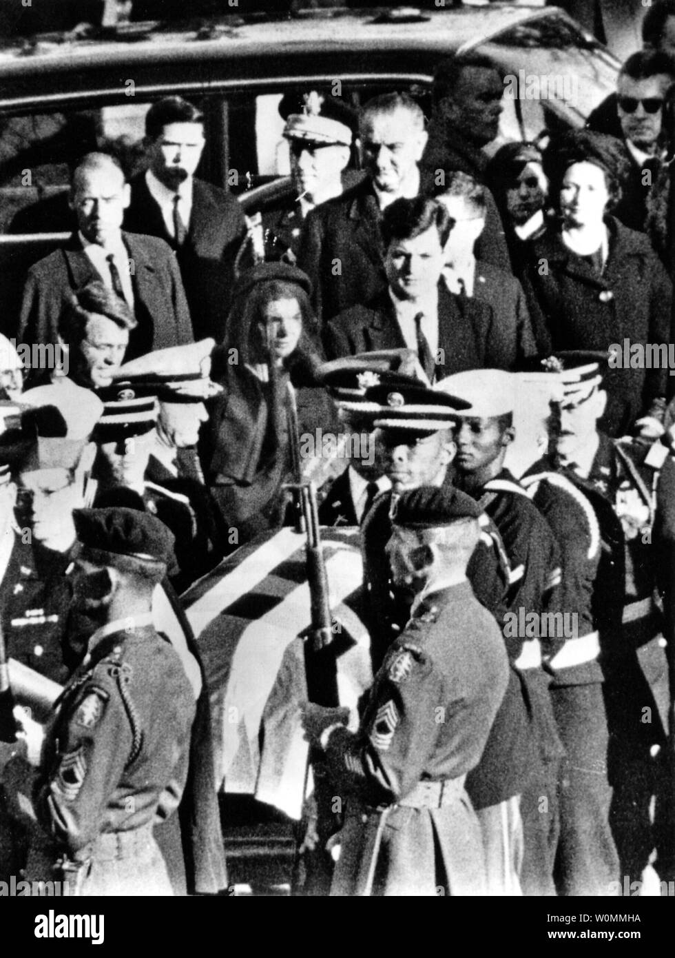 First Lady Jacqueline Kennedy starrt ausdruckslos an den Sarg ihres Mannes Präsident John F. Kennedy, wie es für die Beerdigung auf dem Arlington National Cemetery, 25. November 1963 vorbereitet wird. Der Präsident Brüder, Robert und Edward stehen entweder auf der Seite von Frau Kennedy. Neu vereidigte Präsident Lyndon B. Johnson und seine Frau Lady Bird hinter ihnen gesehen. An diesem Freitag den 50. Jahrestag der Ermordung von Präsident Kennedy am 22. November 1963. UPI/Dateien Stockfoto
