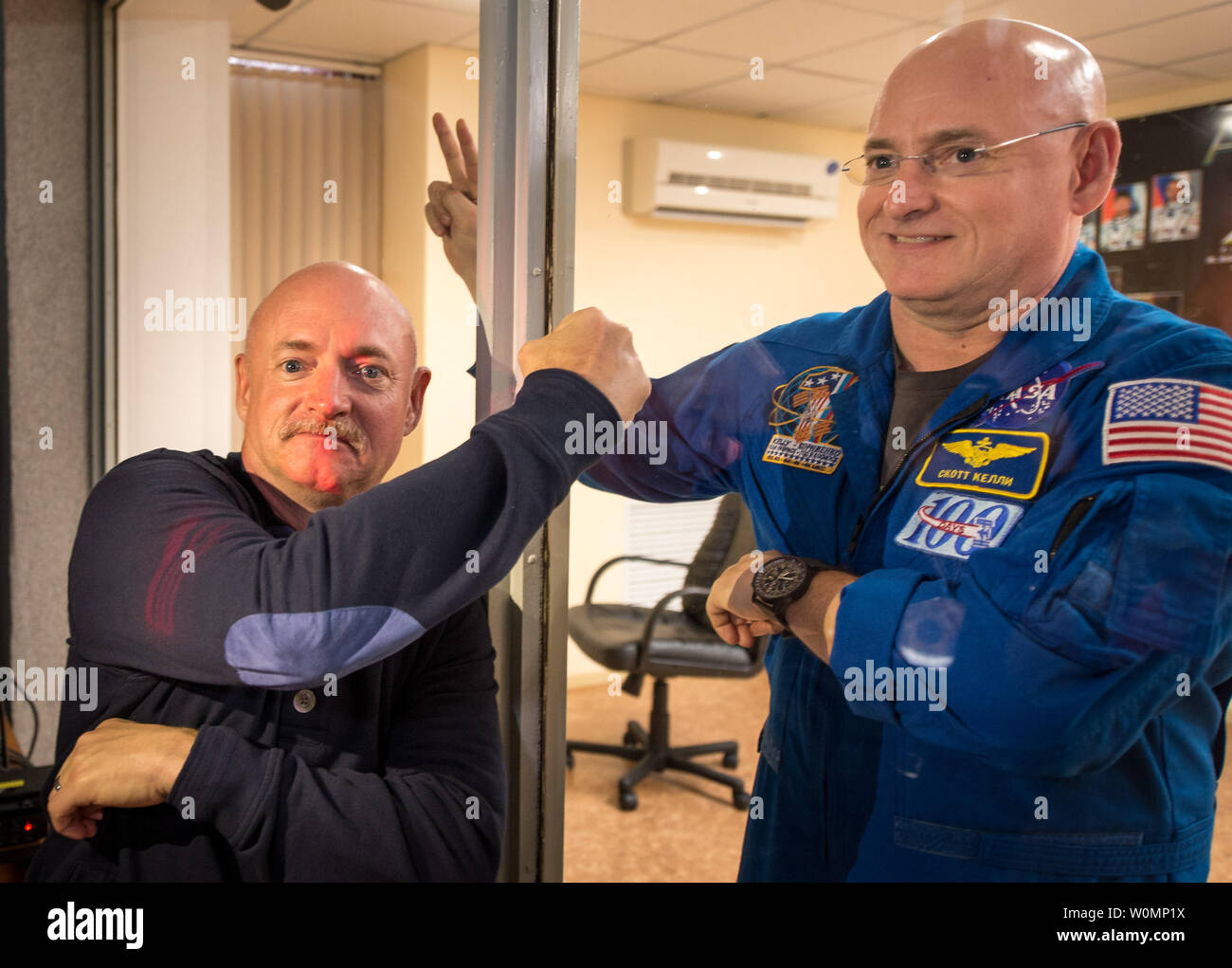 Im Ruhestand der NASA-Astronaut Mark Kelly, Links, Faust pumpt seine Zwillingbruder, NASA-Astronaut Scott Kelly durch Glas wie Scott Kelly und Kollegen crew Gehilfen, russische Kosmonauten Gennadi Padalka, und Michail Kornienko der russischen Föderalen Raumfahrtagentur (Roskosmos) in einer Pressekonferenz teilnehmen, während in der Quarantäne am 26. März 2015, an der Kosmonaut Hotel in Baikonur, Kasachstan. Mark Kelly, der vier Space Shuttle Missionen flog und der letzte Flug des Space Shuttle Endeavour geboten, die in der biomedizinischen Studien auf dem Boden teilnehmen, während seine twin an Bord des Orbiting Laboratory ist. . Stockfoto