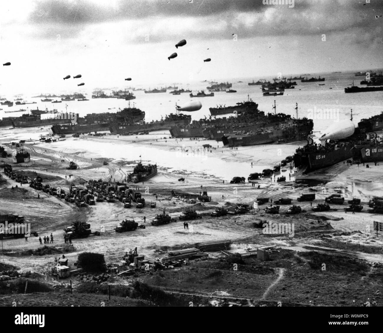 Landenden Schiffe Fracht an Land setzen auf eine der Invasion Strände, bei Ebbe in den ersten Tagen nach der Operation Overlord, Juni 1944. Unter identifizierbaren Schiffe vorhanden sind USS LST-532 (in der Mitte der Ansicht); USS LST LST-262 (3. von rechts); USS LST LST-310 (2. von rechts); USS LST-533 (teilweise sichtbar Ganz rechts) und USS LST-524. Hinweis Barrage balloons Overhead und Armee Half-track Konvoi bilden bis auf den Strand. Foto von der U.S. Coast Guard/National Archives/UPI Stockfoto