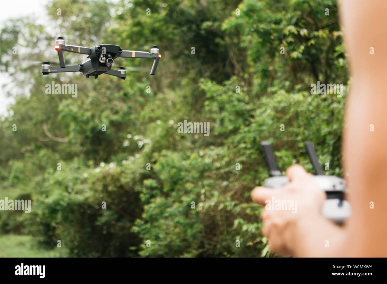 Flying drone auf Fokus und verschwommenes Hände halten eine Fernbedienung Mann in einem Feld Stockfoto