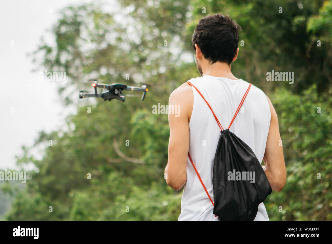Rückansicht eines jungen Mannes Betrieb einer Drohne durch Fernbedienung im Park. Stockfoto