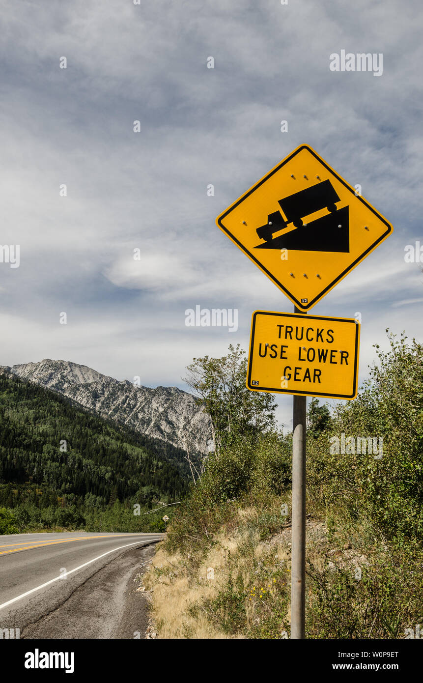 Schild, das die Lkw-Fahrer darauf hinweist, dass die Straße vor dem Fahrzeug steil und bergab sein wird. Berge und Wolken machen die Fahrt schön. Stockfoto