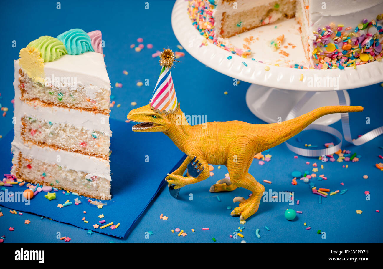 Spielzeug Dinosaurier trägt eine Partei hat neben einem Stück Geburtstagstorte Stockfoto