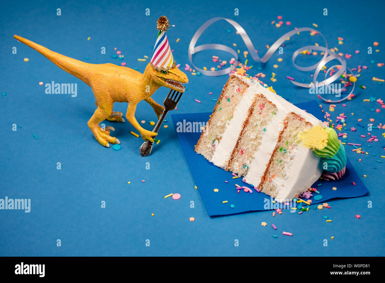Spielzeug Dinosaurier Holding eine Gabel neben einem Stück Torte auf einem blauen Hintergrund. Stockfoto