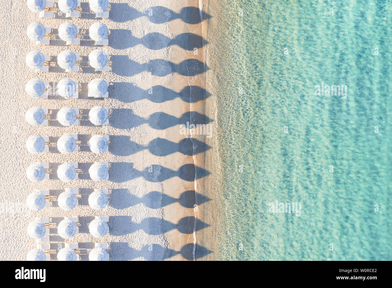 Ansicht von oben, atemberaubenden Blick auf eine erstaunliche leeren weißen Strand mit weißen Sonnenschirmen und türkisklares Wasser während des Sonnenuntergangs. Stockfoto