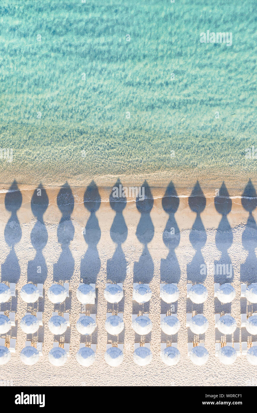 Ansicht von oben, atemberaubenden Blick auf eine erstaunliche leeren weißen Strand mit weißen Sonnenschirmen und türkisklares Wasser während des Sonnenuntergangs. Stockfoto