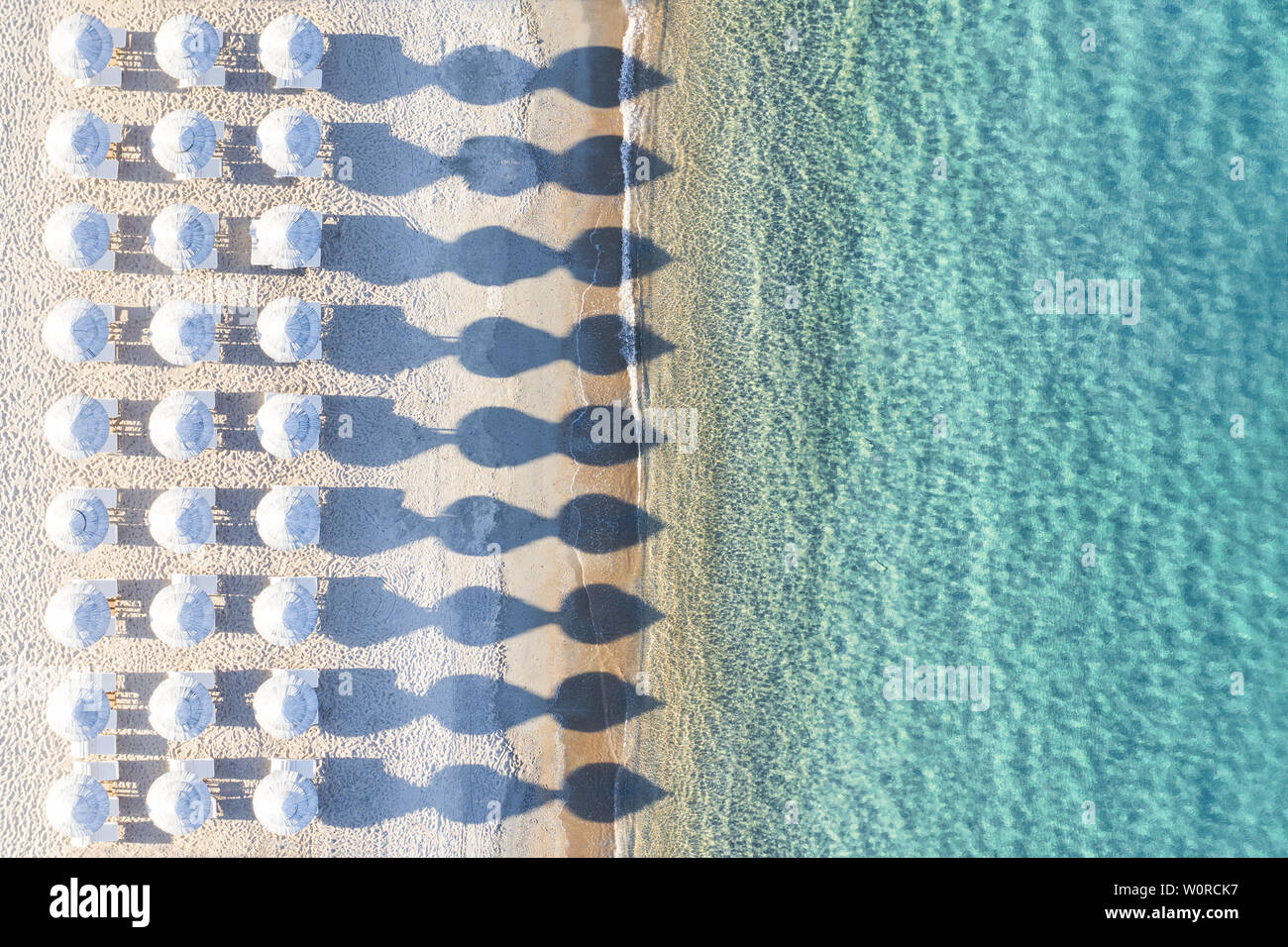 Ansicht von oben, atemberaubenden Blick auf eine erstaunliche leeren weißen Strand mit weißen Sonnenschirmen und türkisklares Wasser während des Sonnenuntergangs. Stockfoto