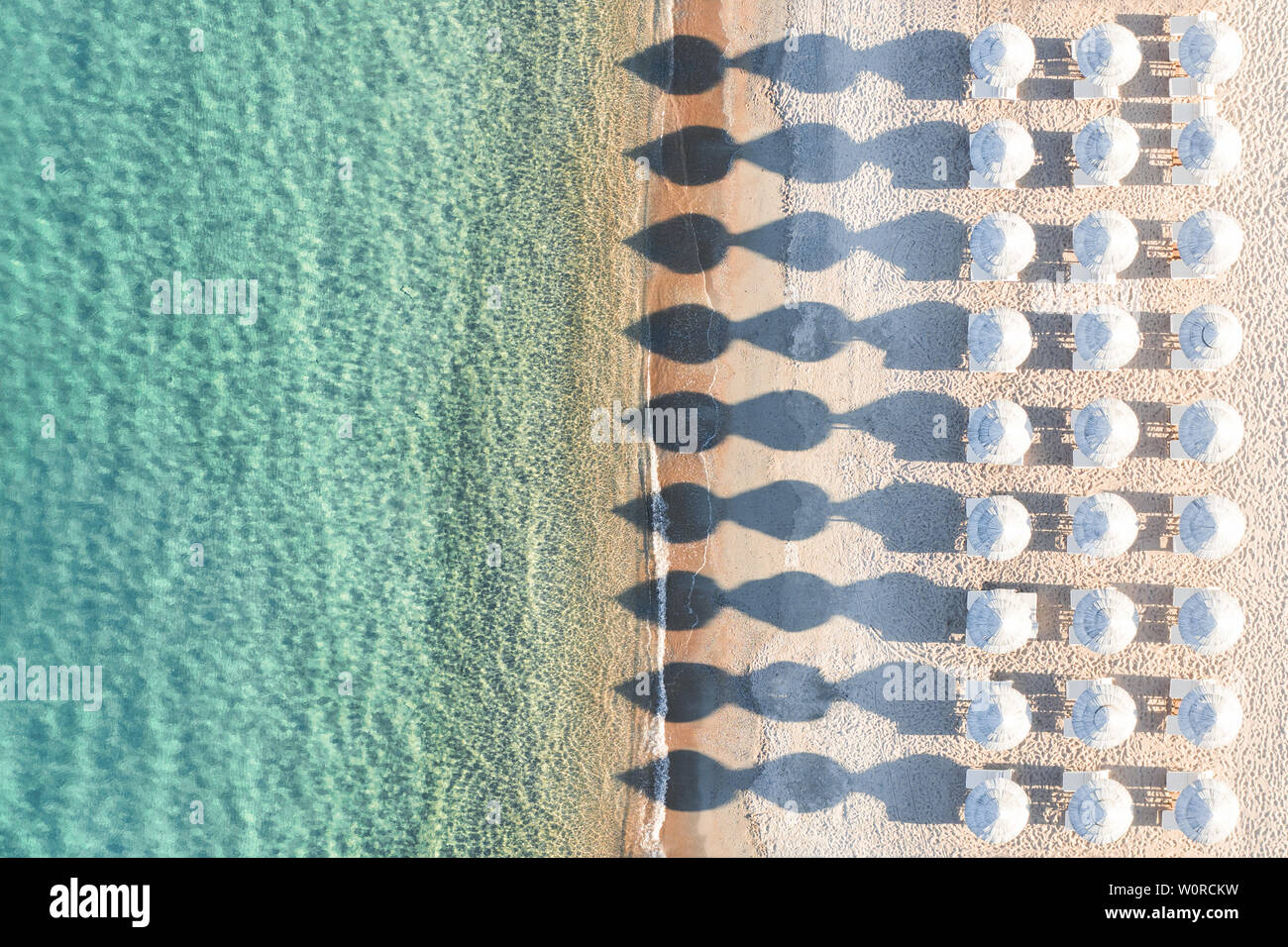 Ansicht von oben, atemberaubenden Blick auf eine erstaunliche leeren weißen Strand mit weißen Sonnenschirmen und türkisklares Wasser während des Sonnenuntergangs. Stockfoto